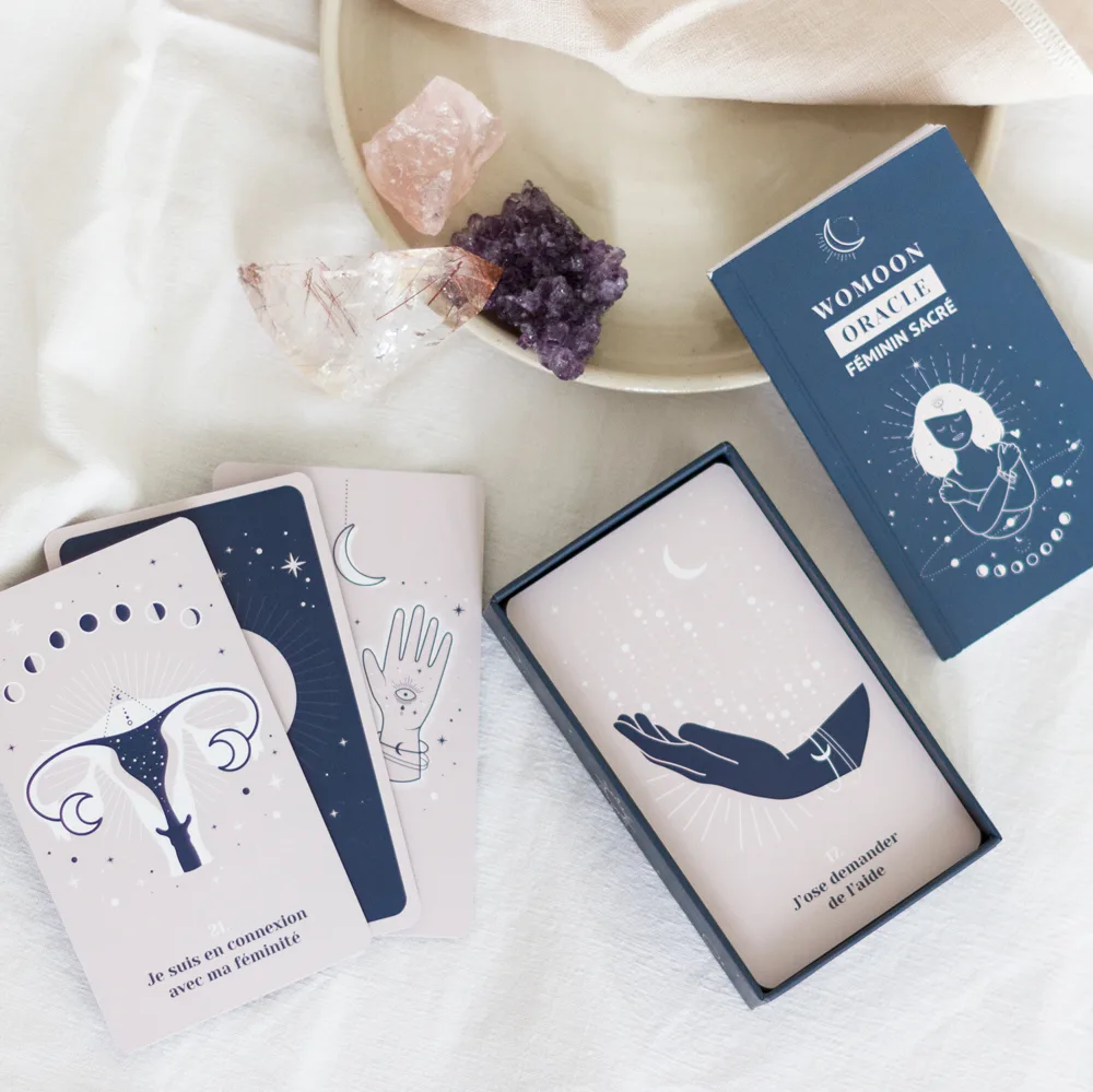 Cartes de l'oracle Womoon Féminin sacré posées à côté de leur boîte et de pierres